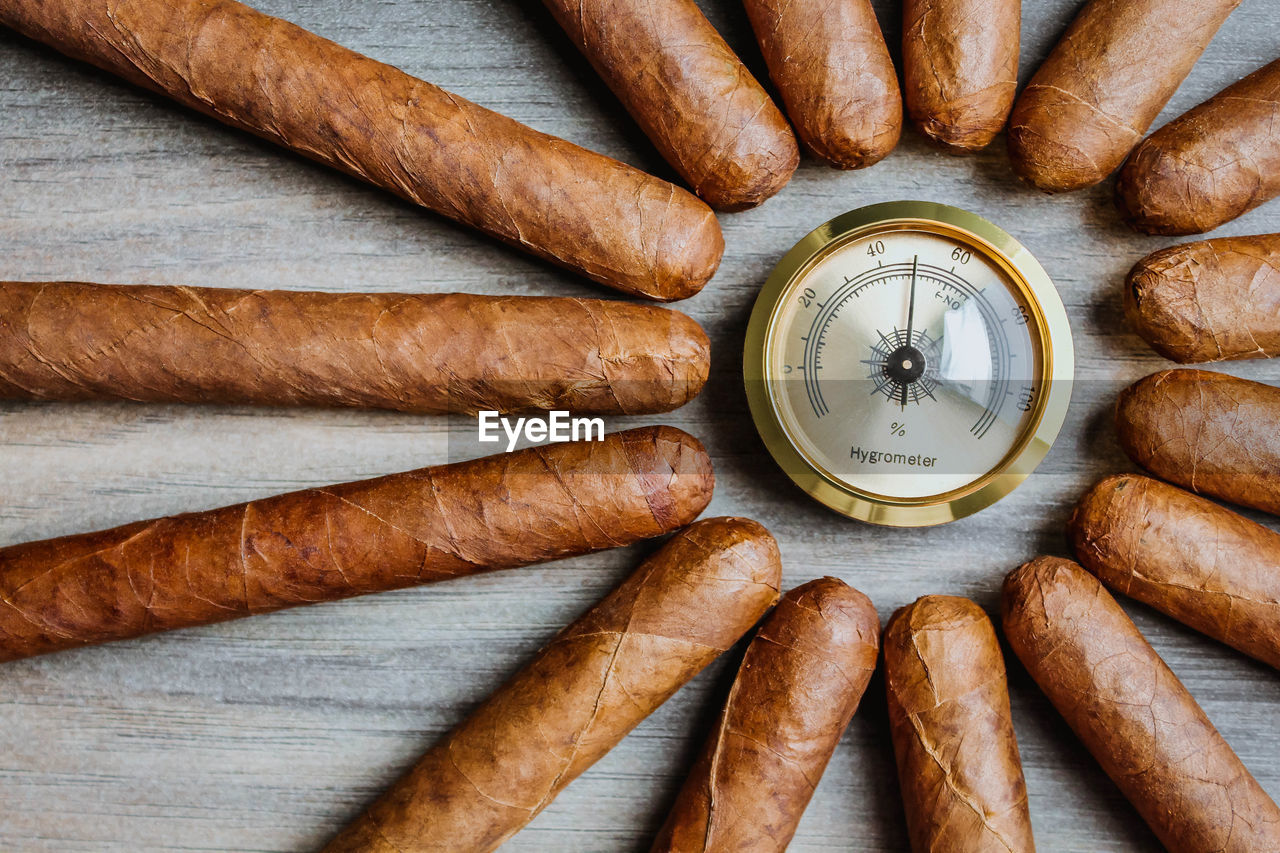 High angle view of cigars with humidor hygrometer on the wooden background