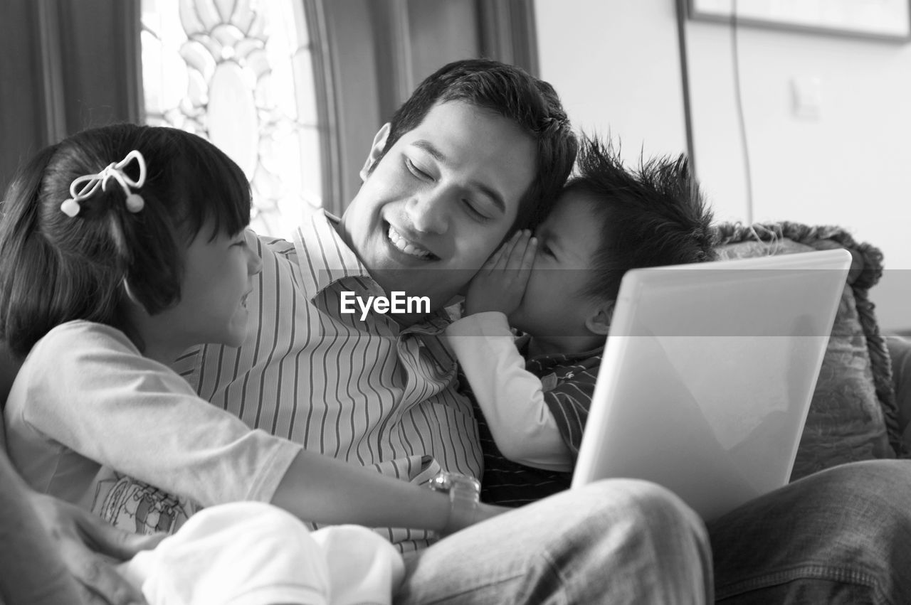 Father with children using laptop on sofa at home