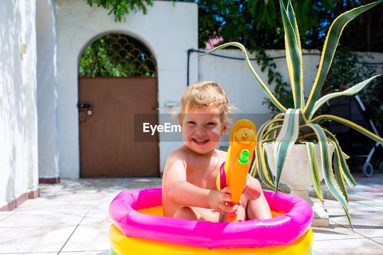 Cute baby is having fun in an inflatable pool with a water gun in summer.