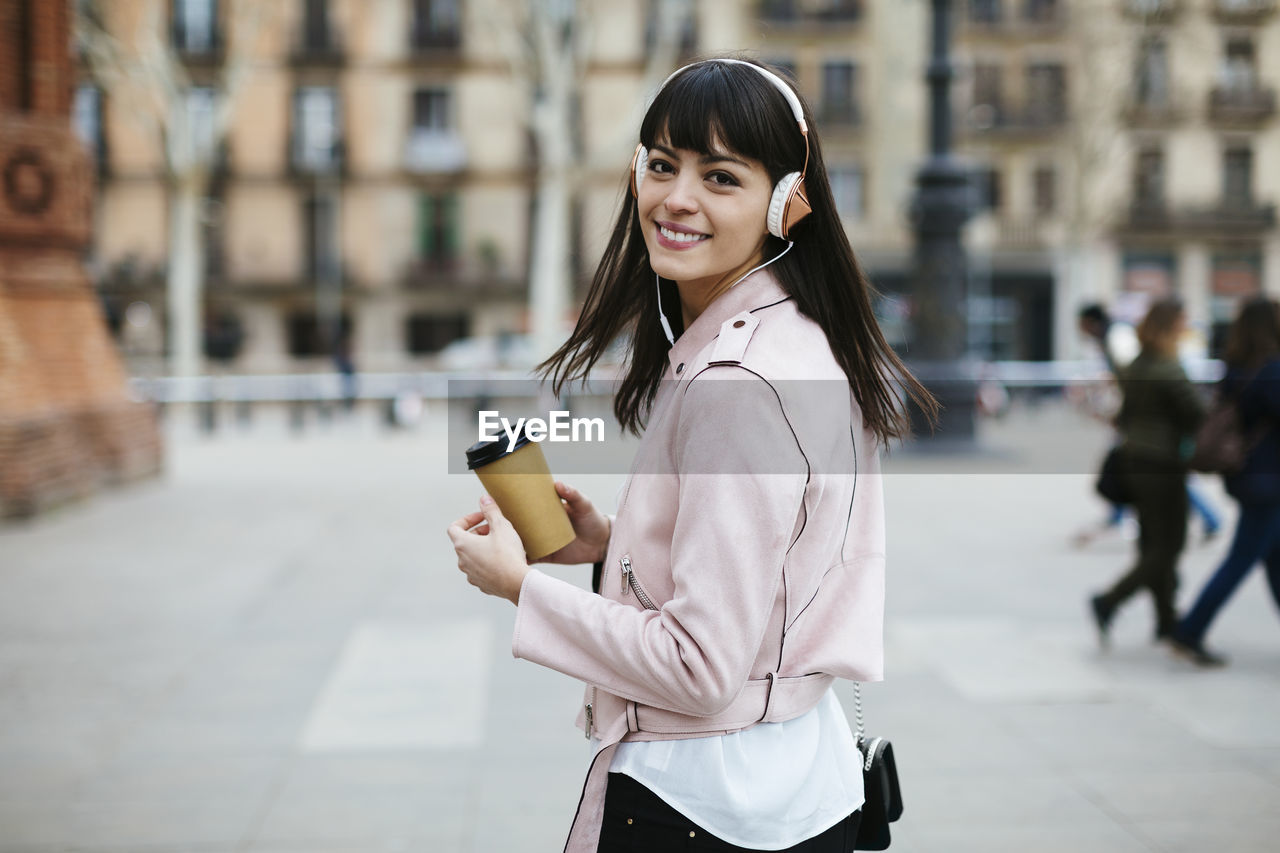 Spain, barcelona, smiling woman with coffee and headphones in the city