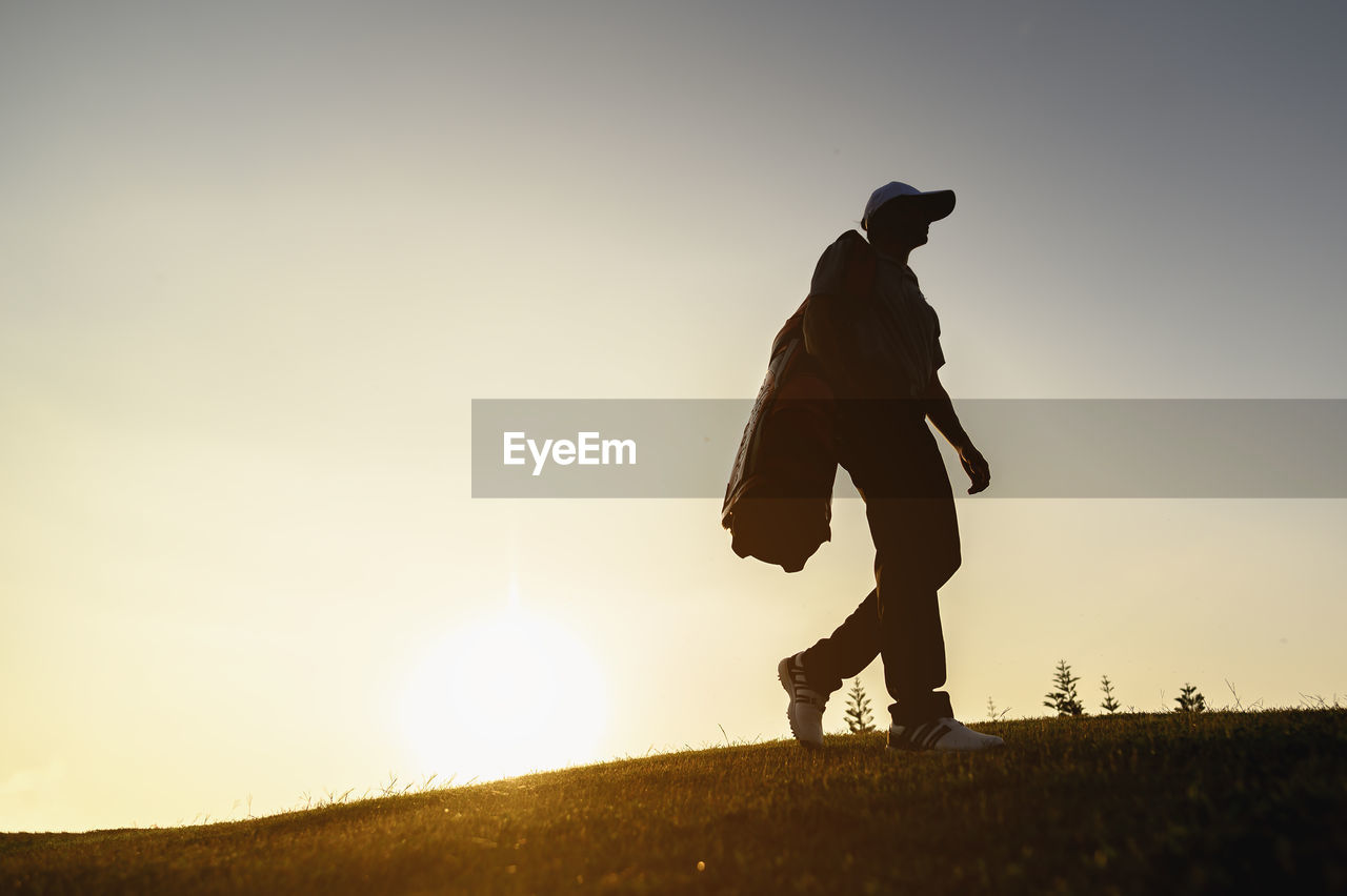 Low angle view of silhouette man walking on land against clear sky during sunset