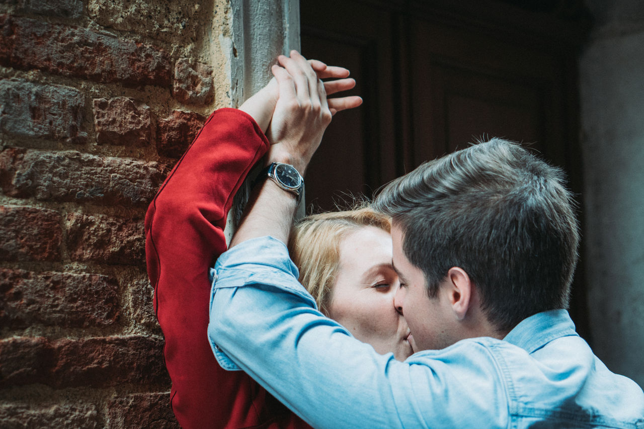 Young couple holding hands while kissing against wall