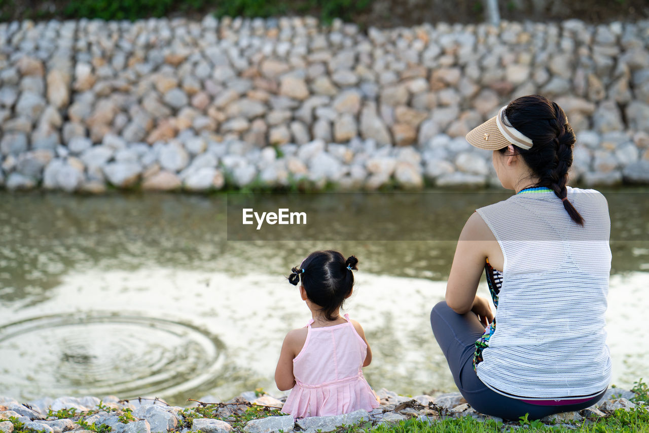 Adorable girl sitting at pond with her mother in summer.