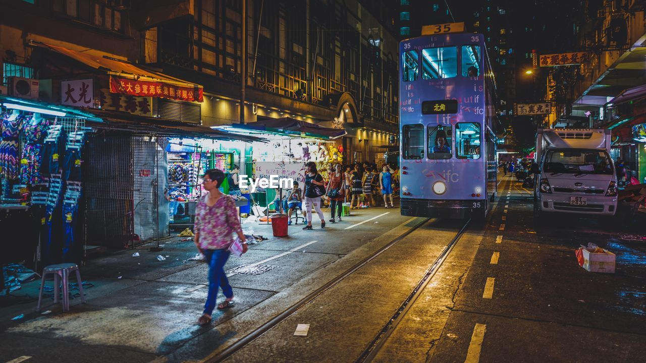 Woman walking on city street by cable car at night