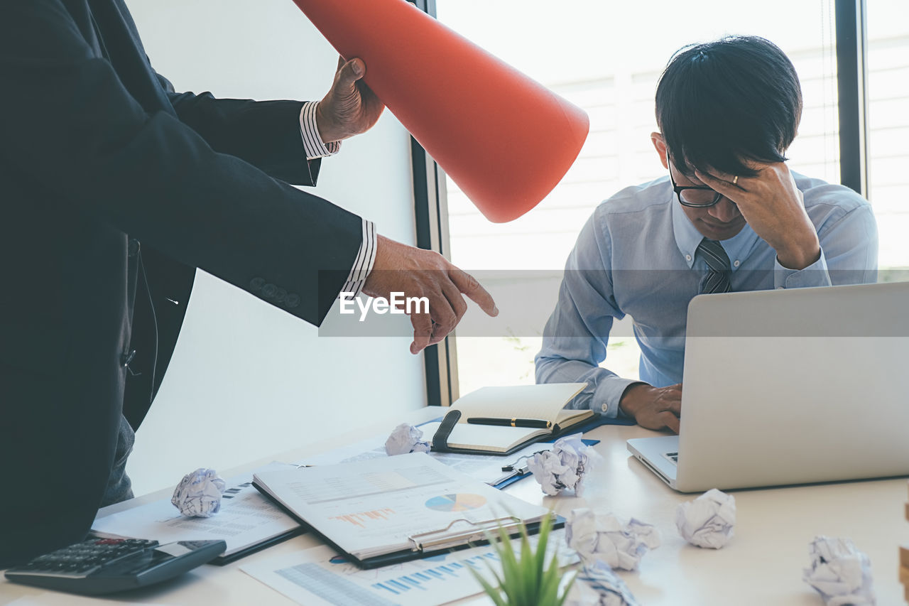 Midsection of businessman scolding stressed colleague at office