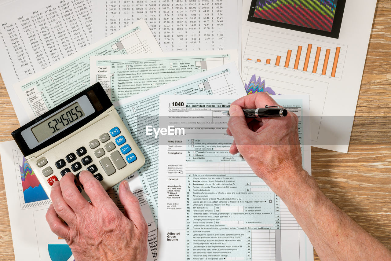 Cropped hands of man filing documents using calculator at table