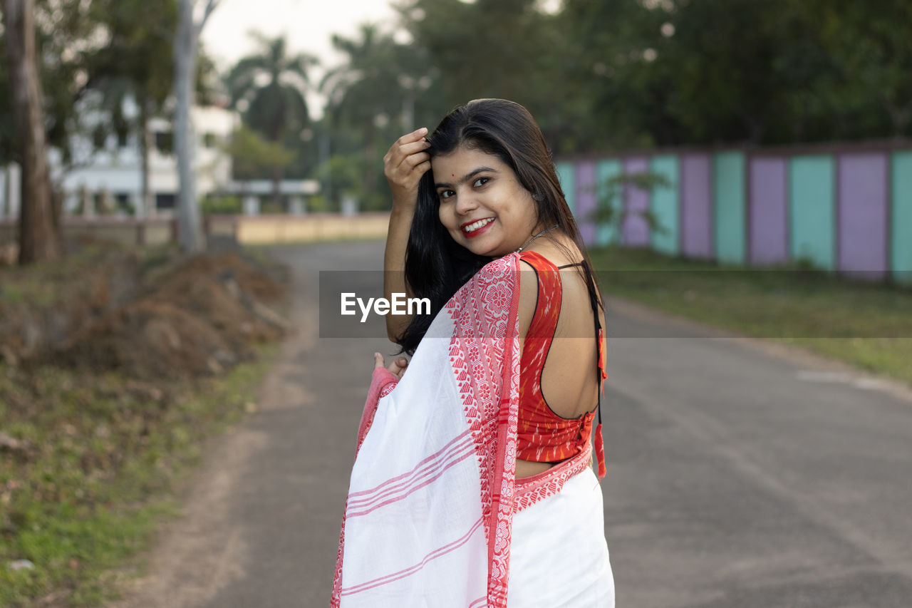 A pretty indian woman in red saree and long hair posing for camera on road