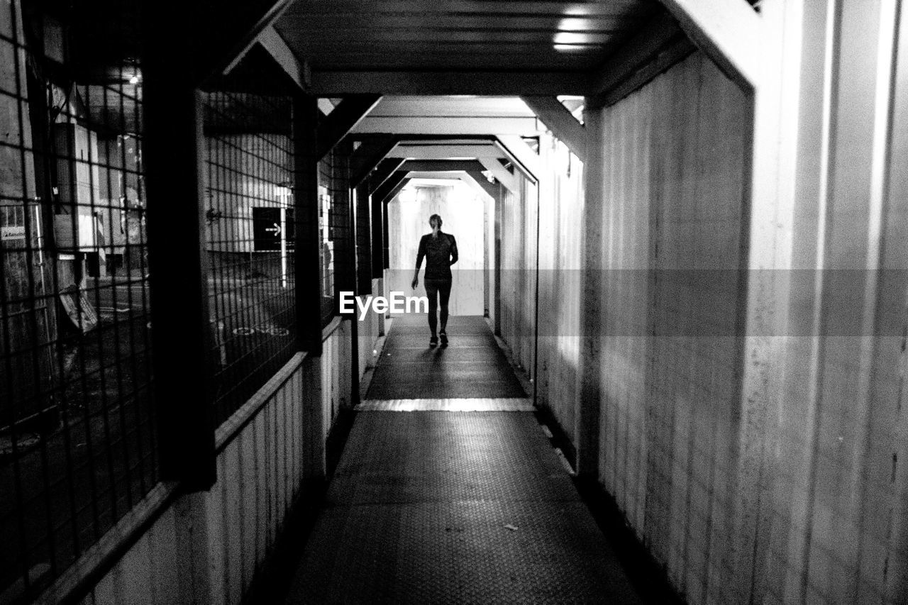 REAR VIEW OF MAN WALKING IN ILLUMINATED TUNNEL