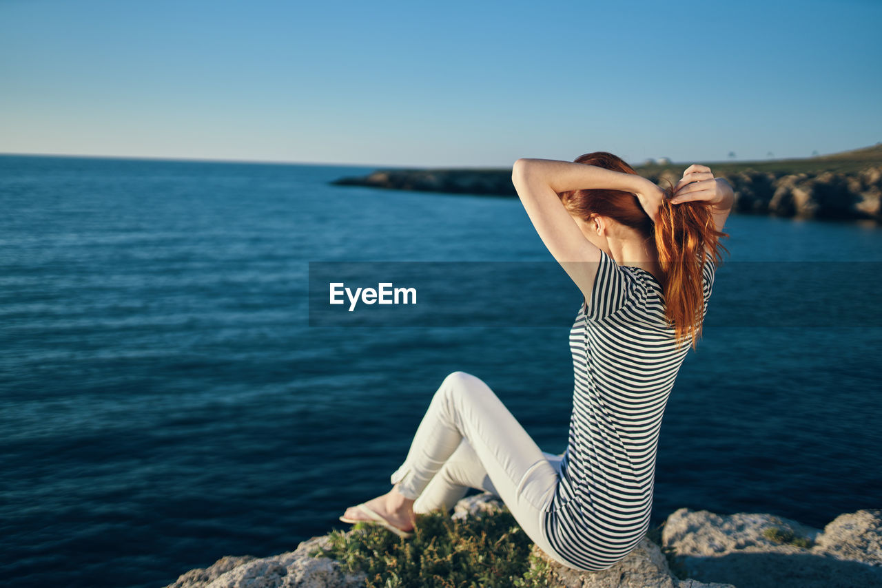 Woman on rock by sea against sky