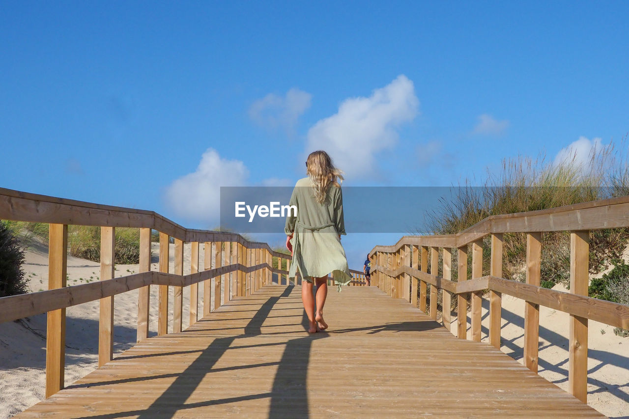 FULL LENGTH OF WOMAN STANDING BY RAILING AGAINST SKY