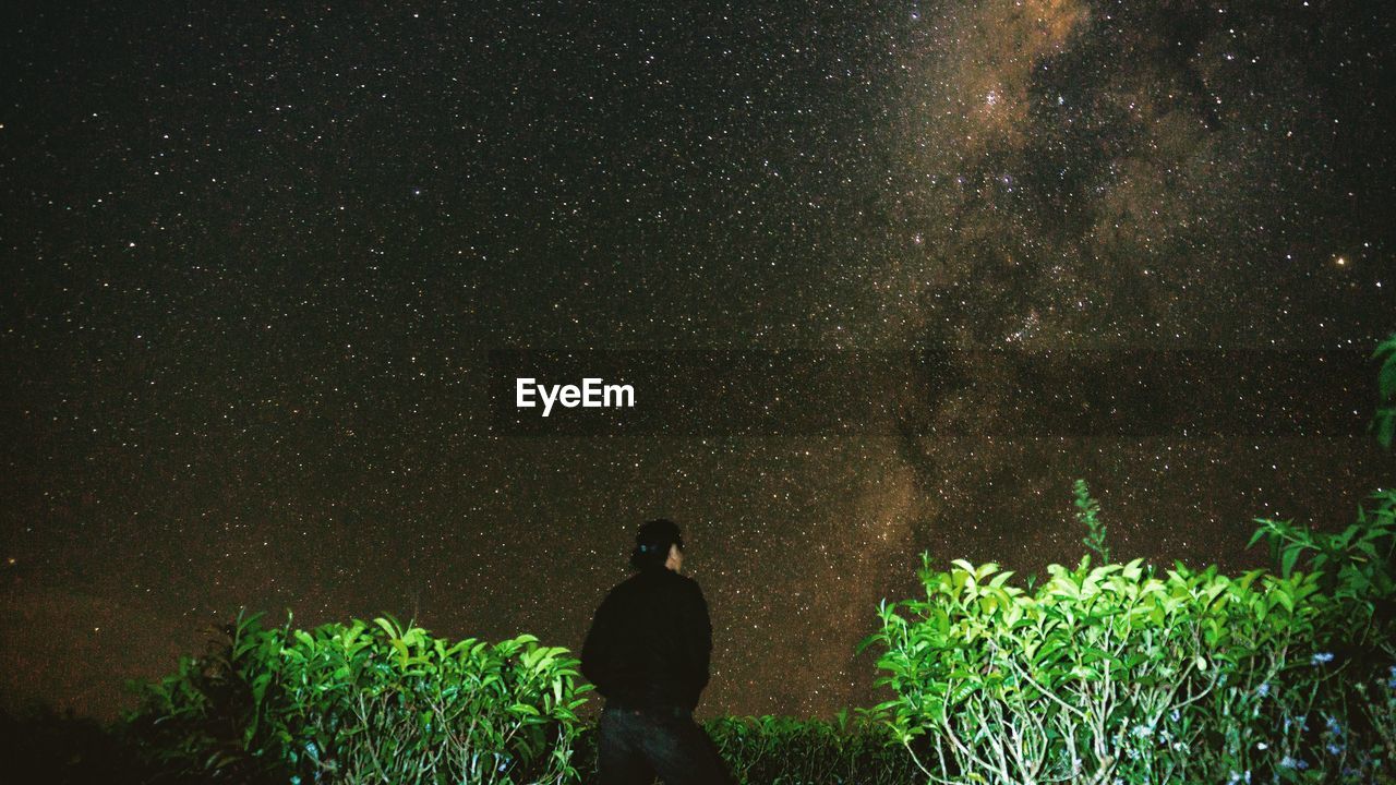 Rear view of man standing against sky at night