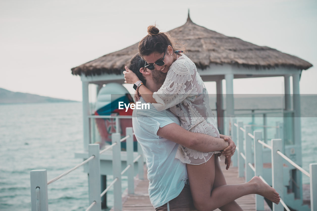 Loving boyfriend carrying girlfriend while standing on pier