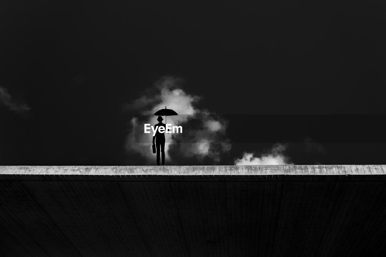 SILHOUETTE MAN STANDING ON RAILING AGAINST SKY