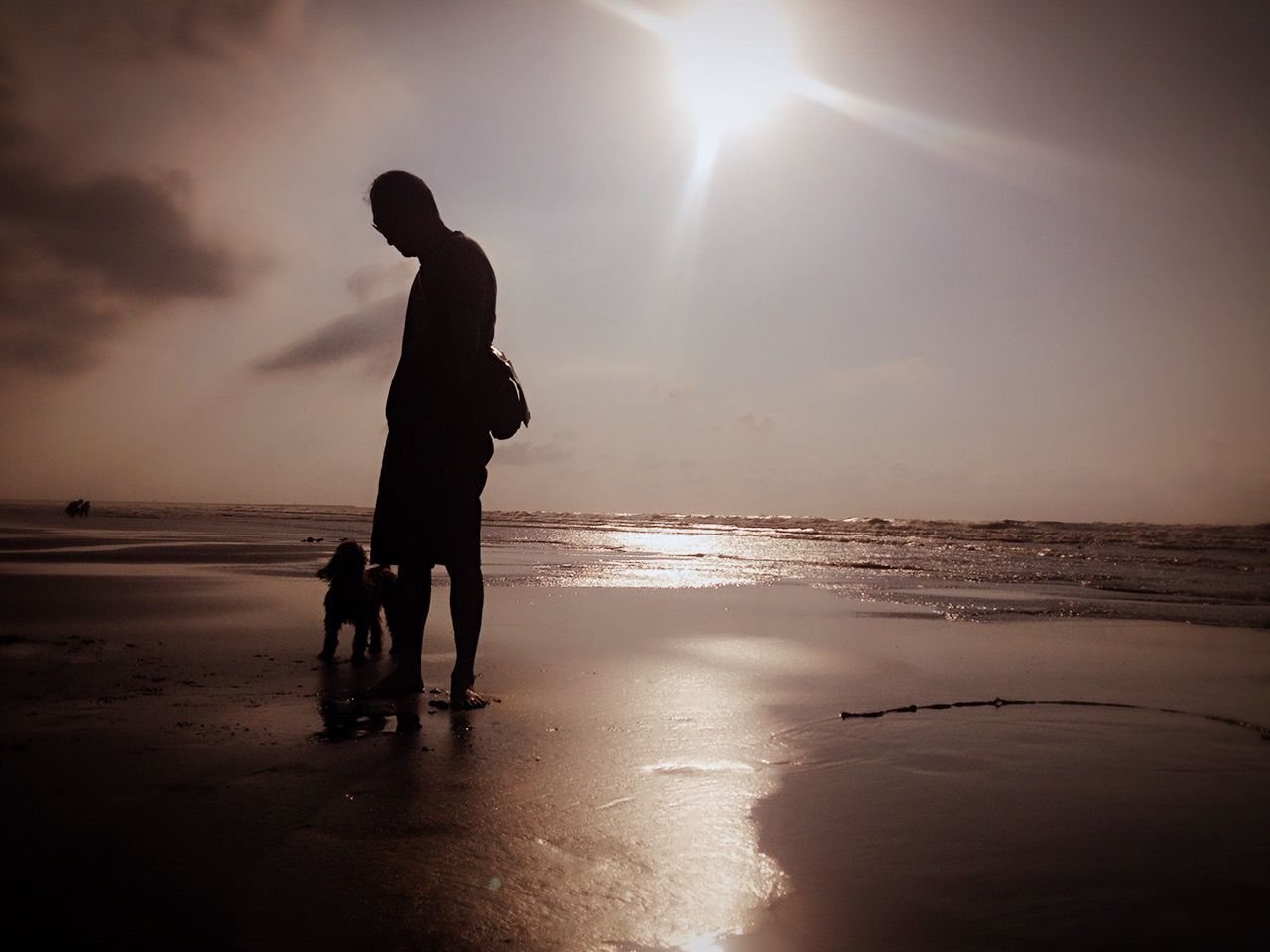 Man standing with dog on beach against sky during sunset