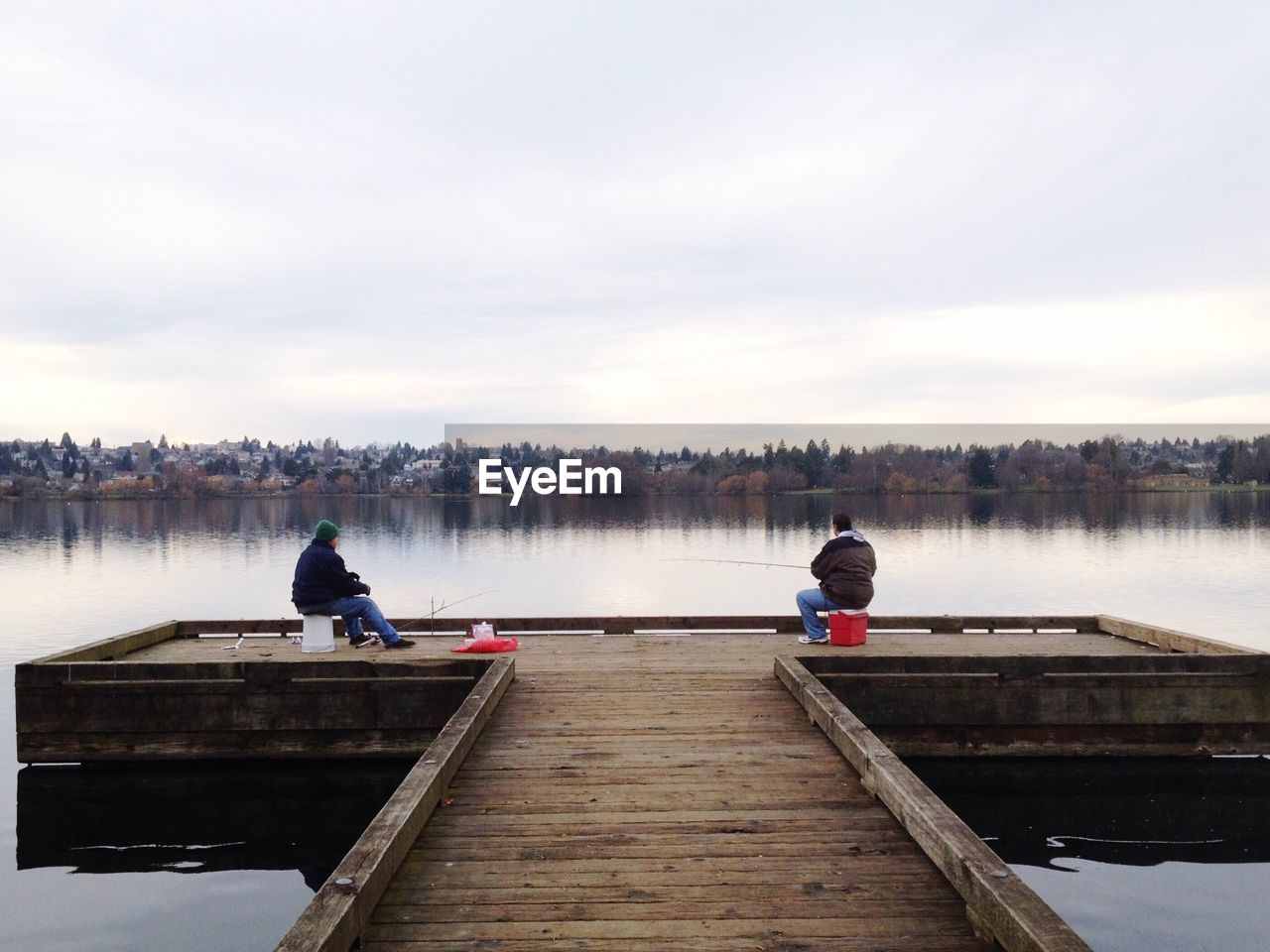 Full length of people fishing on pier by lake against sky