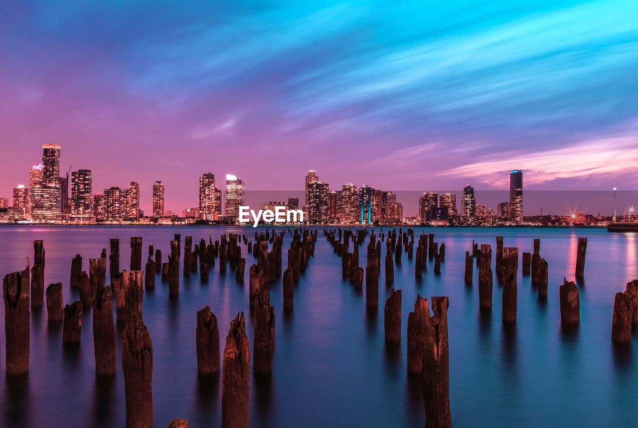 Wooden posts in sea against illuminated skyline