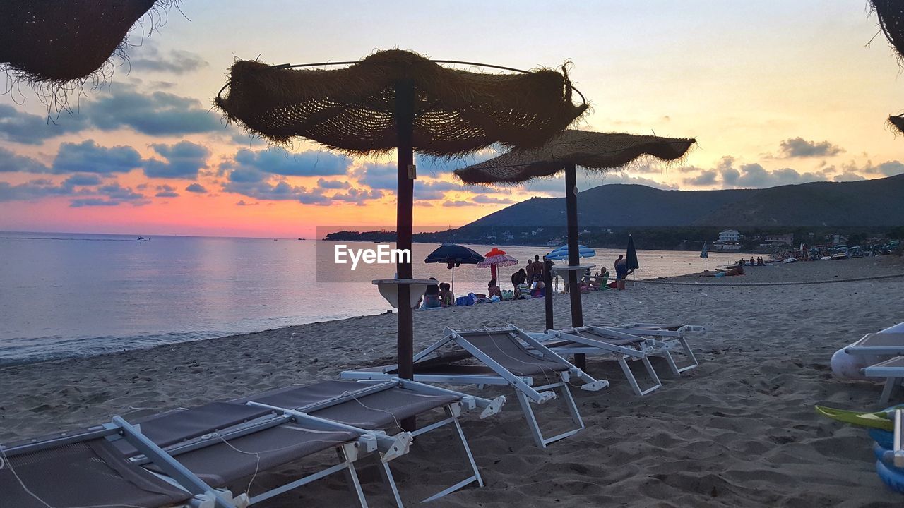 DECK CHAIRS ON BEACH AGAINST SKY AT SUNSET