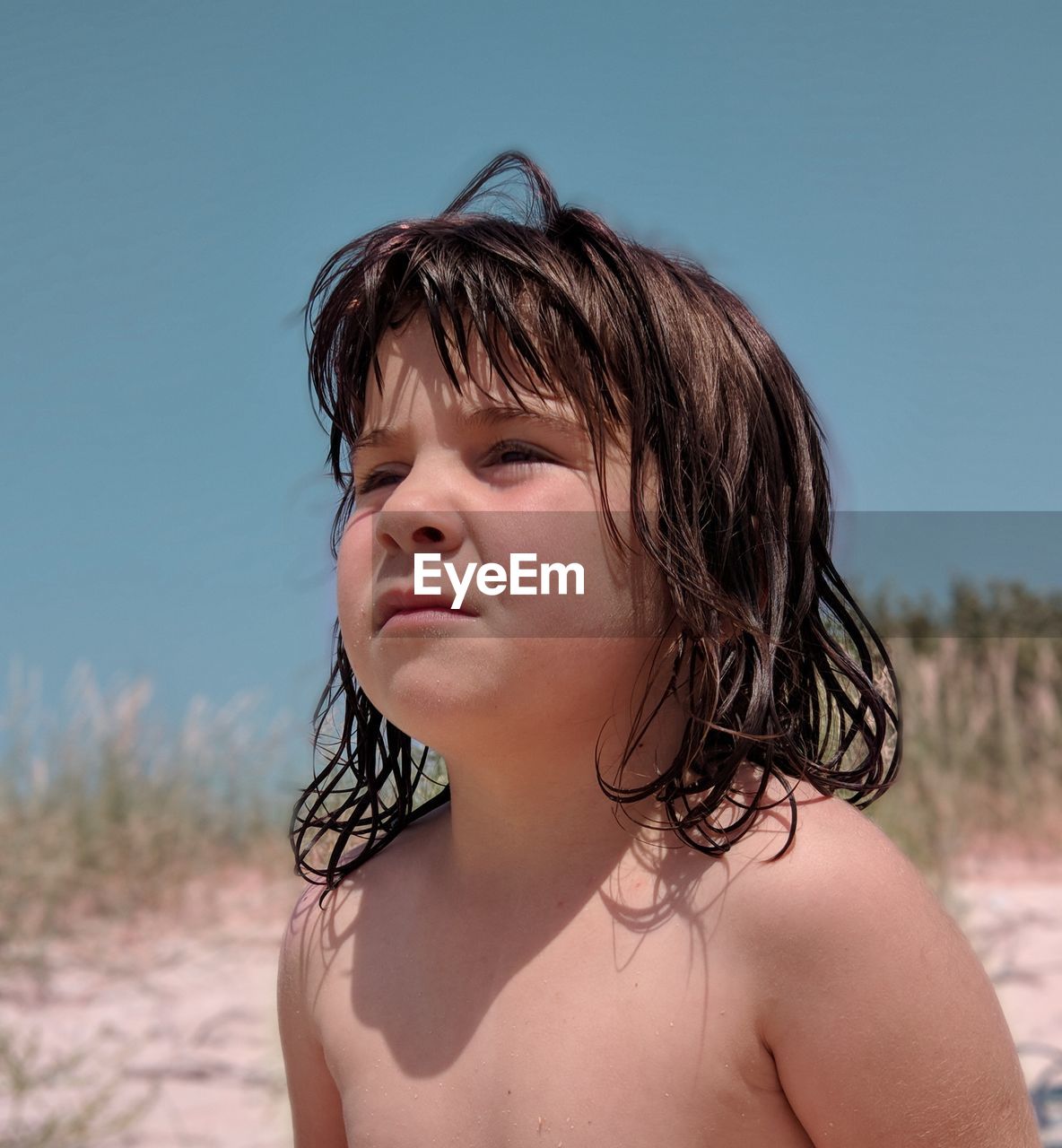 Close-up of shirtless girl looking away at beach against clear sky during sunny day