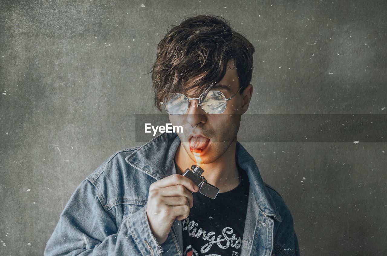 PORTRAIT OF A YOUNG MAN WEARING EYEGLASSES HOLDING CAMERA