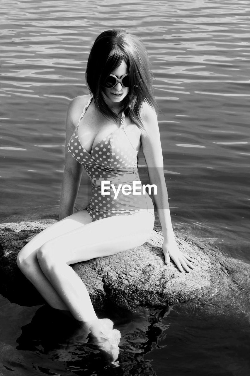 Beautiful woman sitting on rock against sea