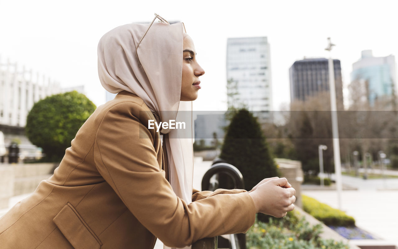 Young woman wearing hijab leaning on railing at office park