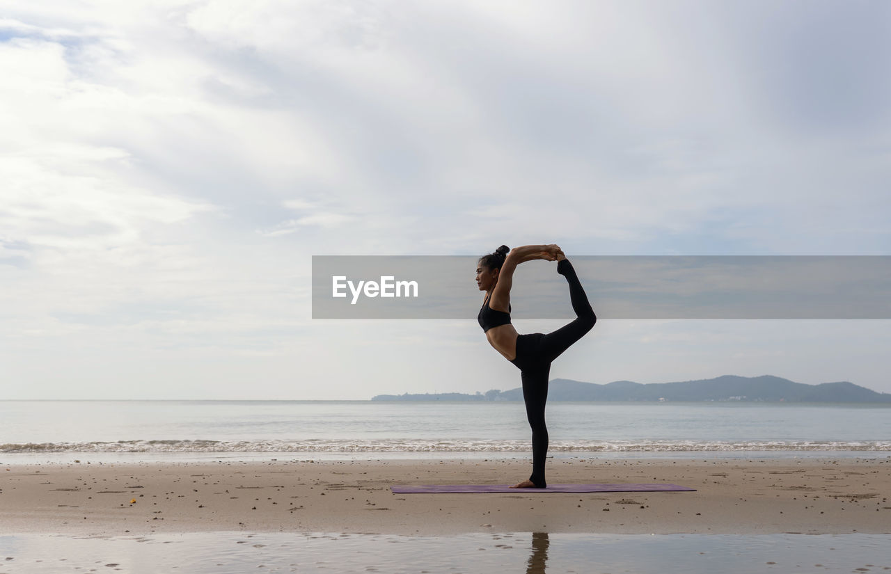 Full length of woman performing yoga on beach against sky