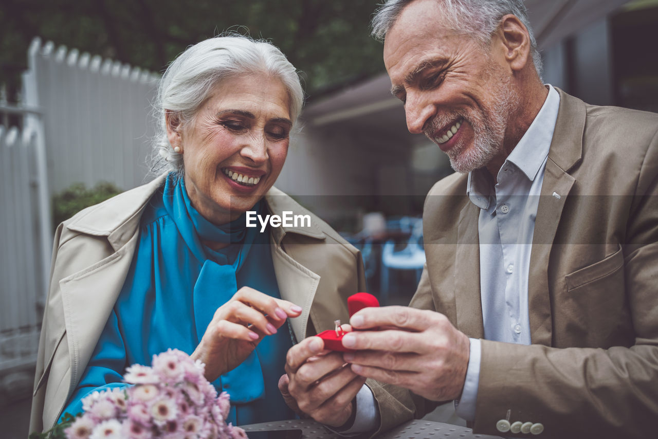 Smiling senior man giving ring to wife while sitting at cafe