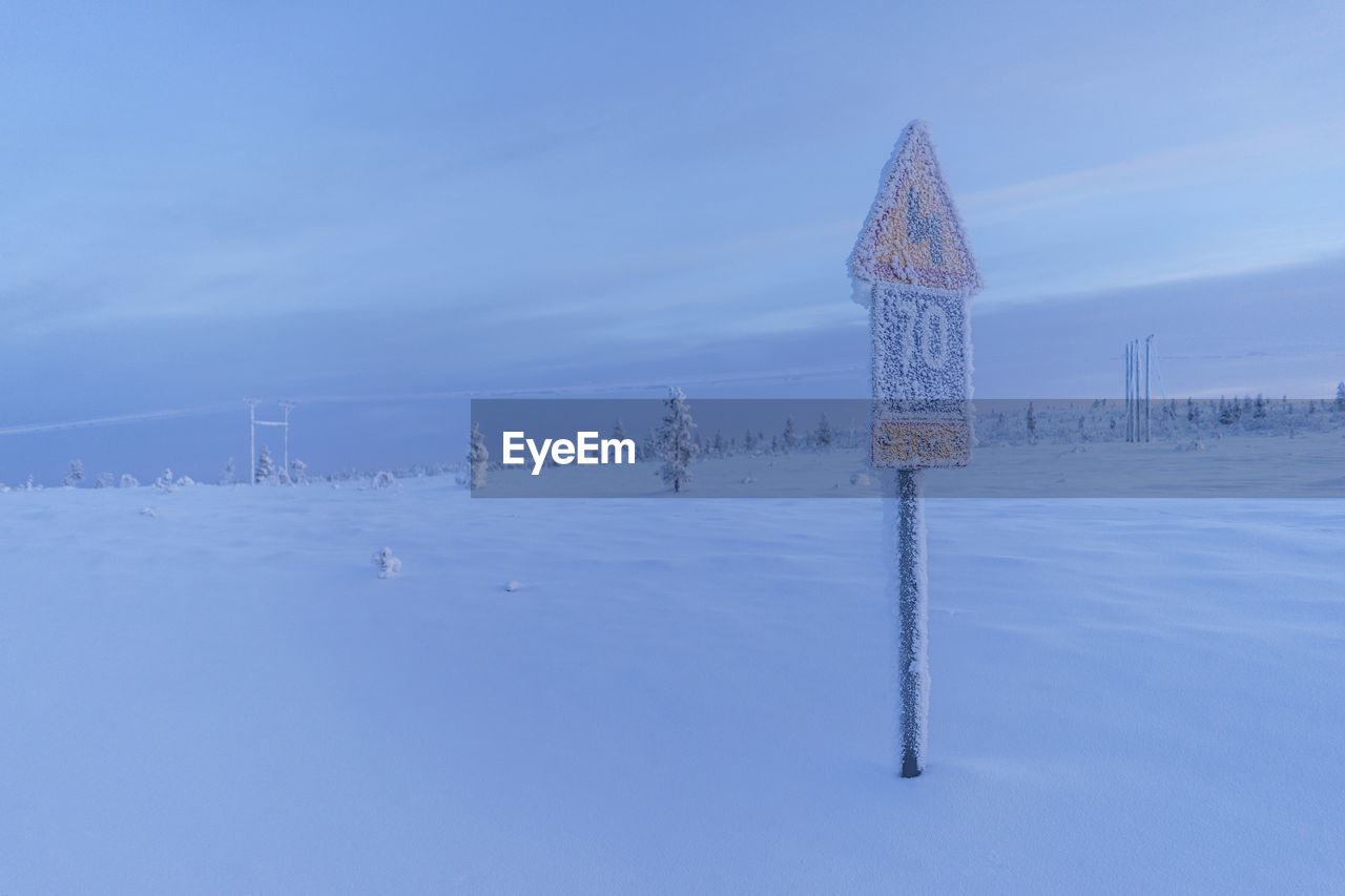 Snow covered road sign against cloudy sky at dusk