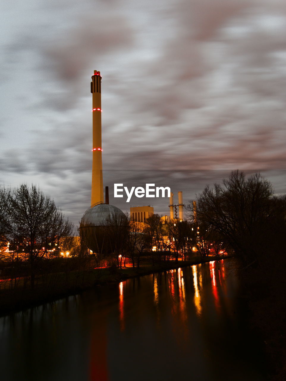 VIEW OF FACTORY BY RIVER AGAINST SKY DURING SUNSET