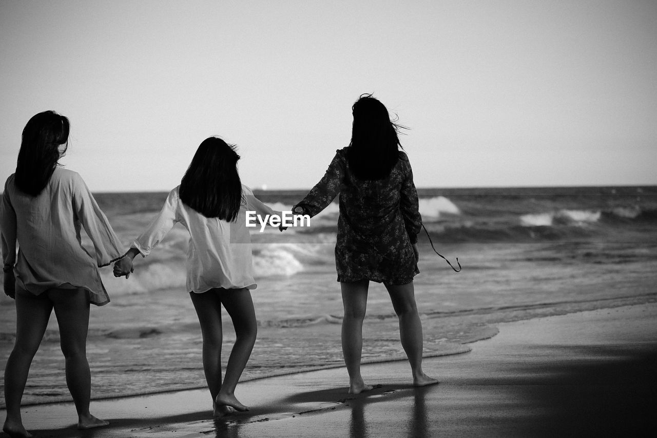 Rear view of friends standing at beach against sky