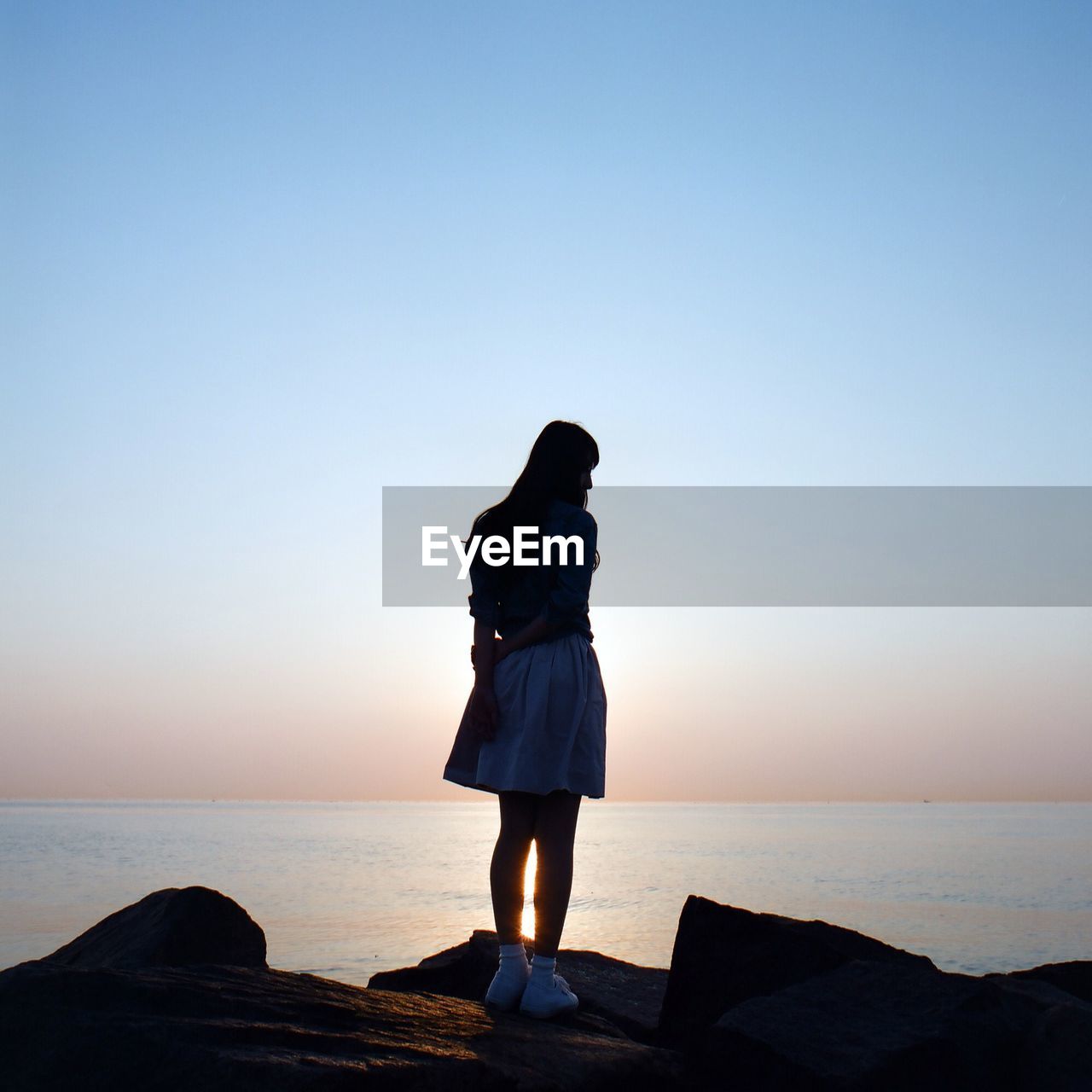 Full length of woman standing on rock by sea against sky during sunset