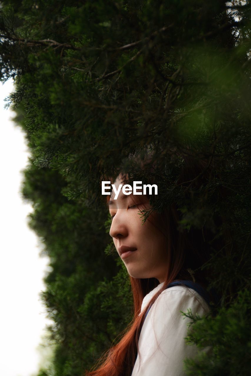 Young woman with eyes closed against plants