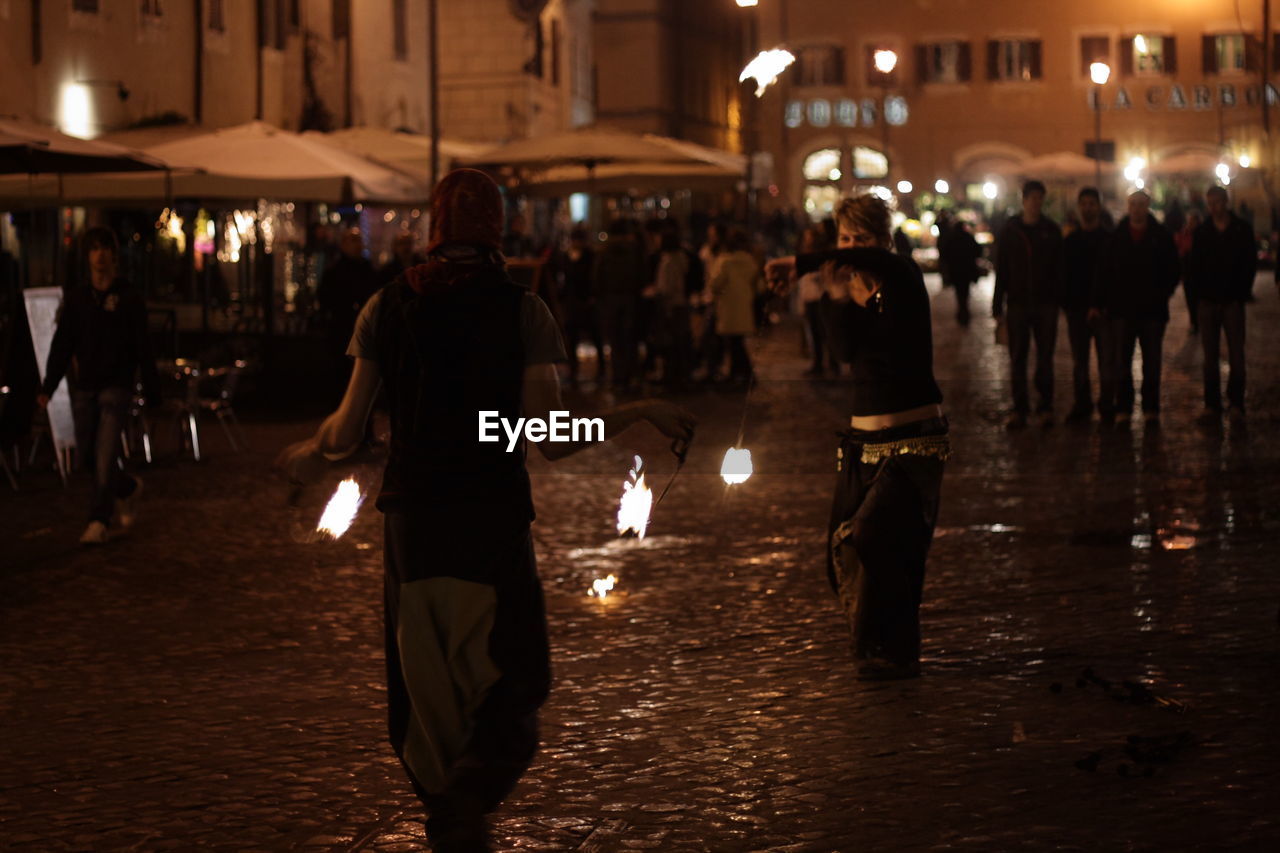 PEOPLE WALKING ON ILLUMINATED STREET AT NIGHT IN CITY