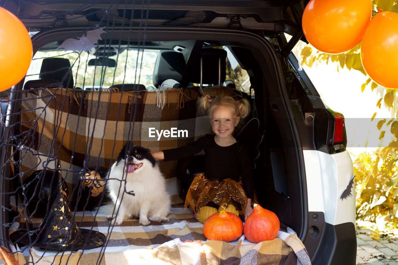 Portrait of cute girl sitting with dog in car trunk