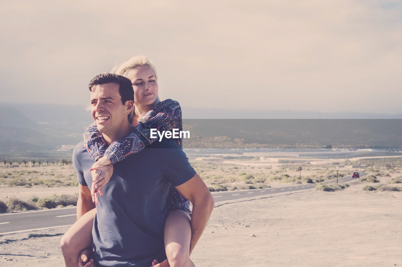 Man carrying woman while standing at beach against sky