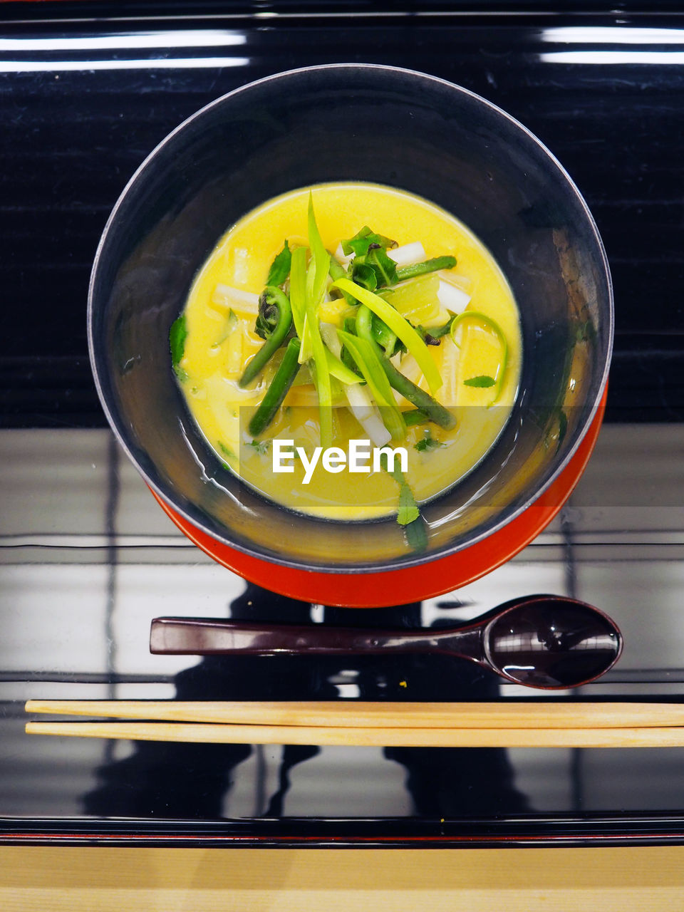 Directly above view of fresh soup served in bowl with spoon and chopsticks on table at restaurant