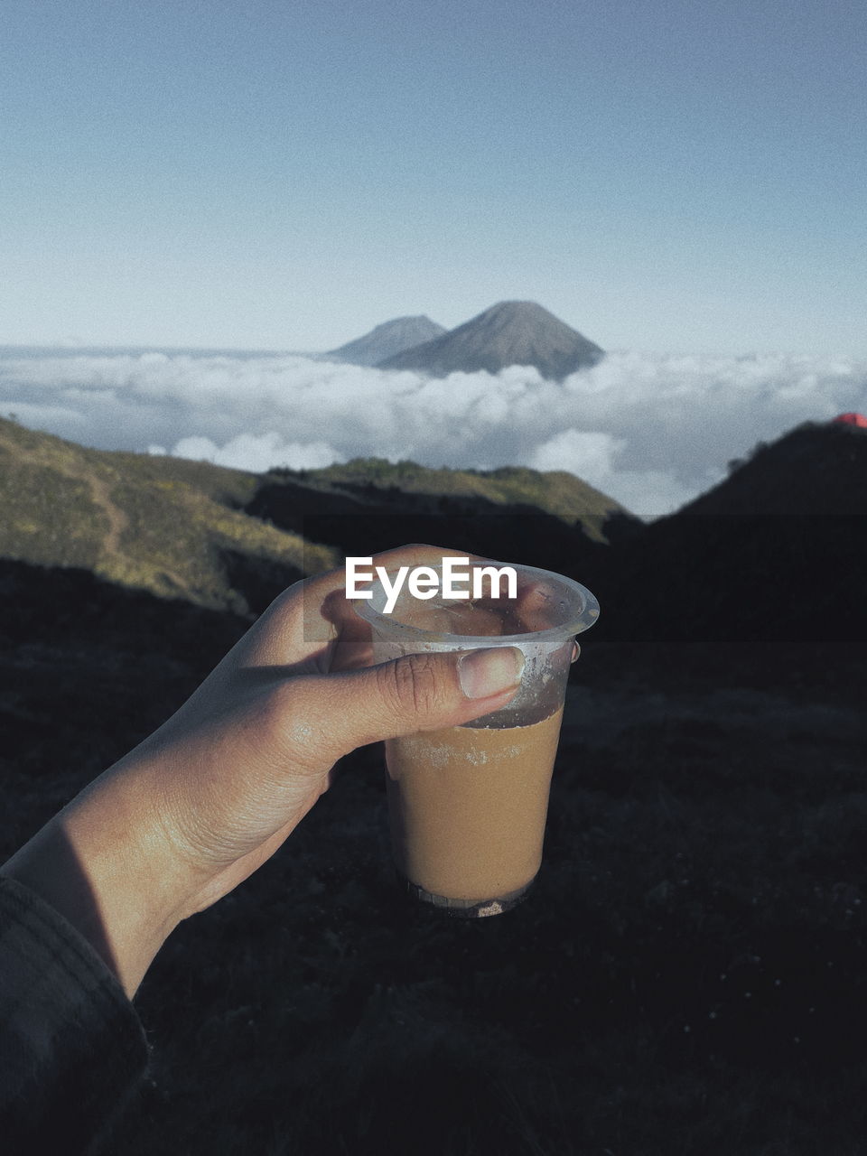 Midsection of person holding coffe  against mountain range