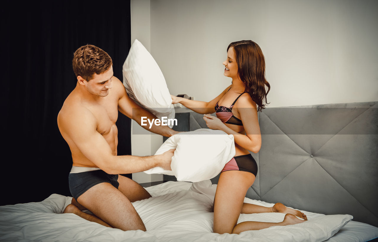 Young couple pillow fighting while kneeling on bed at home