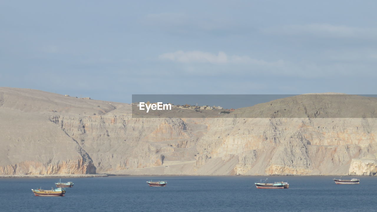 Boats moving in sea against cloudy sky