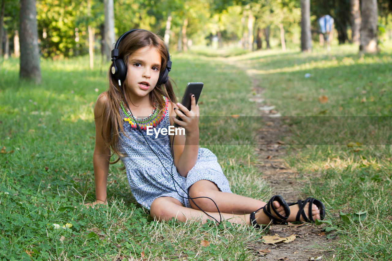 Full length of girl using mobile phone sitting at park