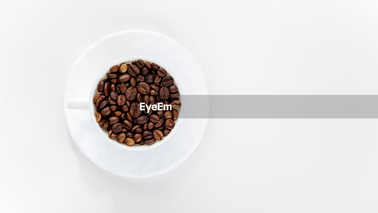 Directly above shot of roasted coffee beans in cup on white background