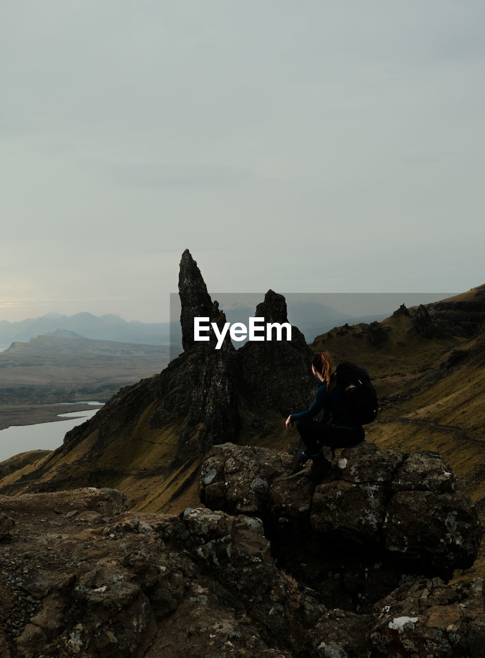 rear view of man sitting on rock against sky
