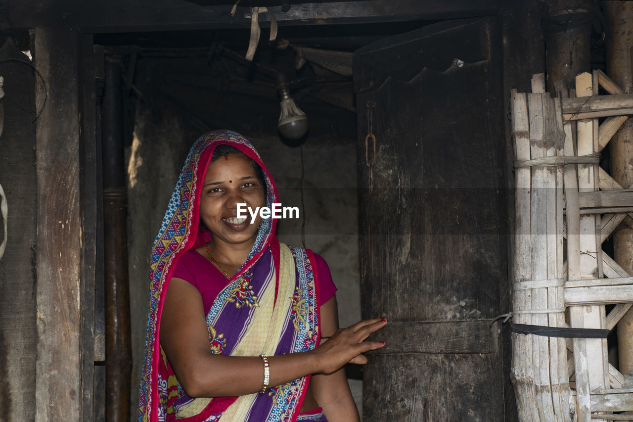 Smiling young woman wearing sari while standing by door in house at village