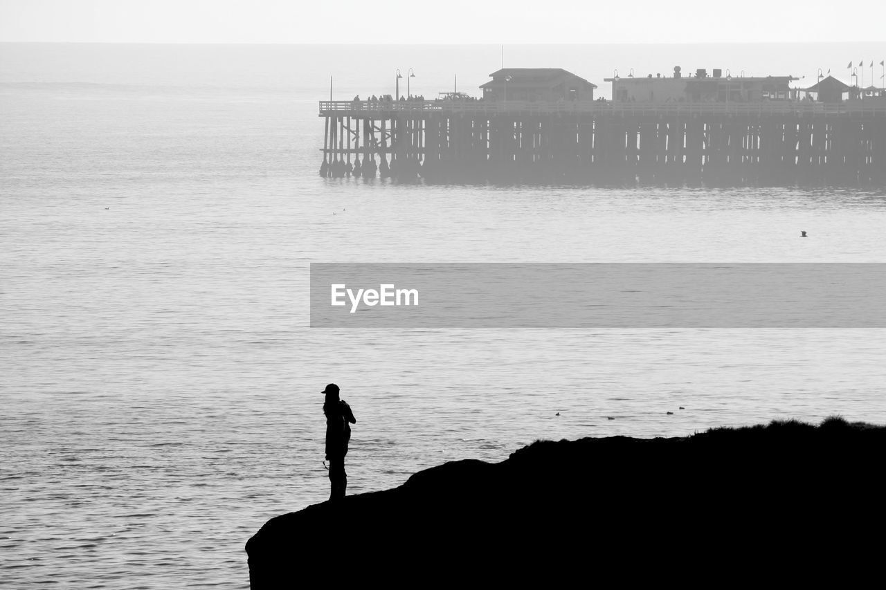 Rear view of silhouette person standing on rock against sea