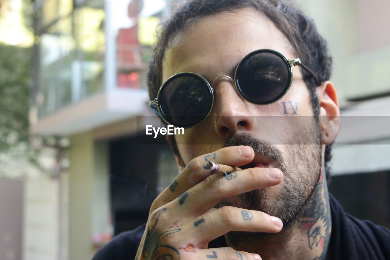 Close-up portrait of man wearing sunglasses smoking cigarette