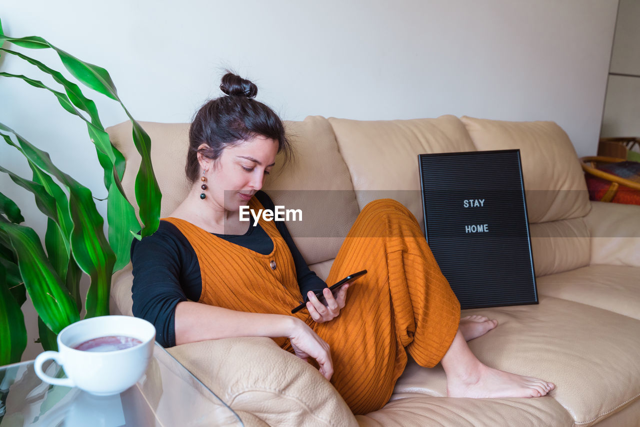 Woman with phone sitting on sofa at home