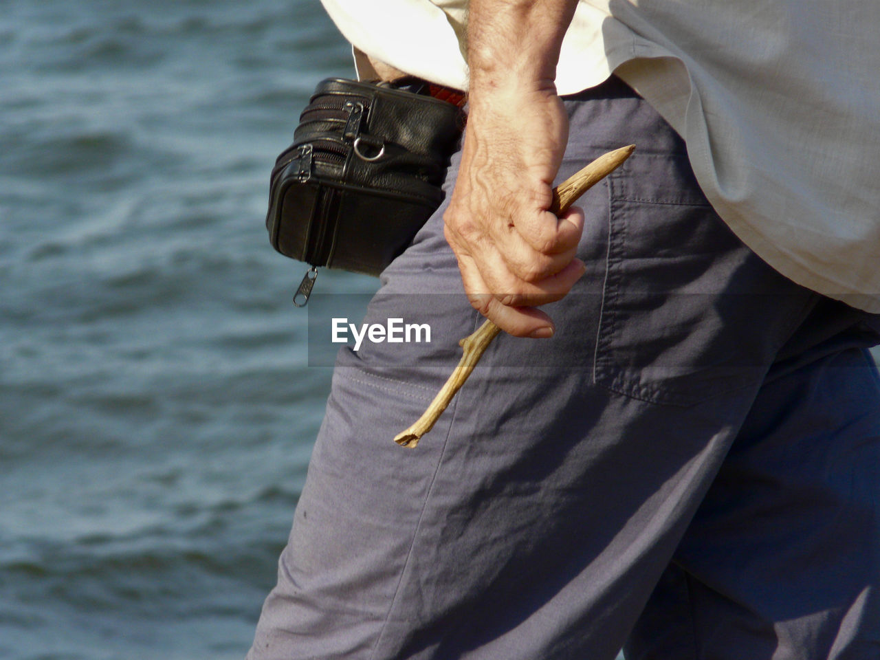 Midsection of man holding stick while standing by sea