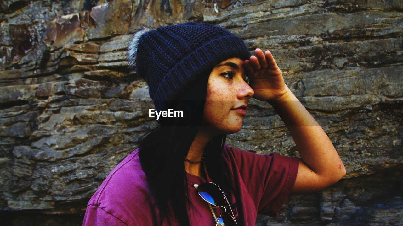 Young woman shielding while looking away against rock formation