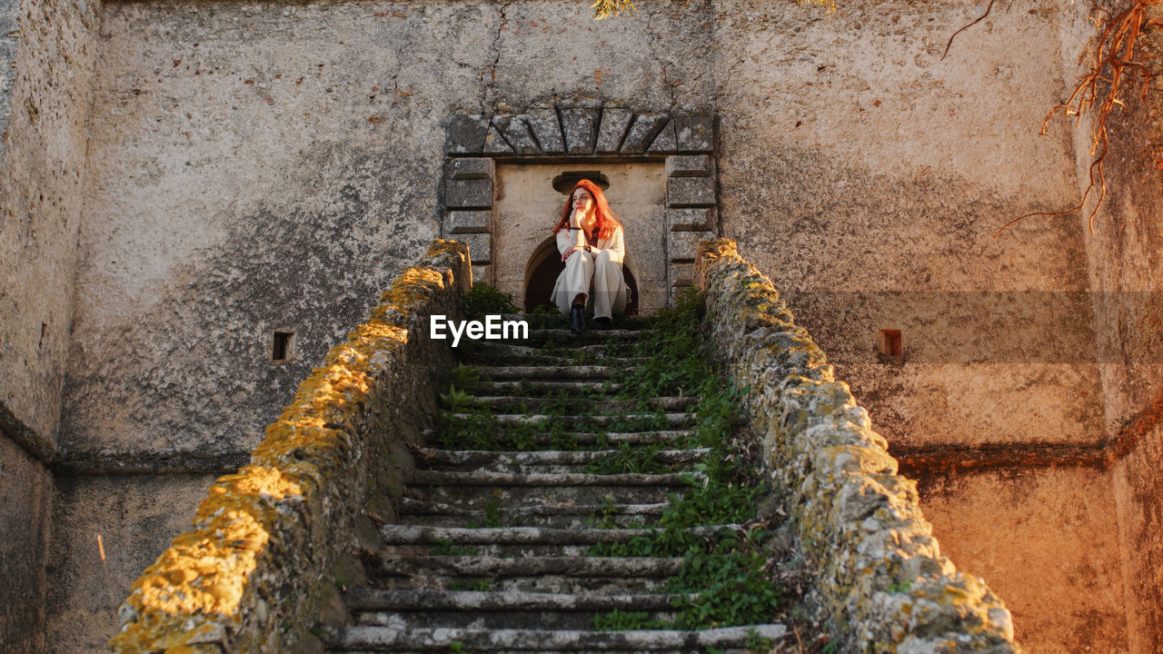 Beautiful girl with white dress sitting on the main entrance stairs of castle