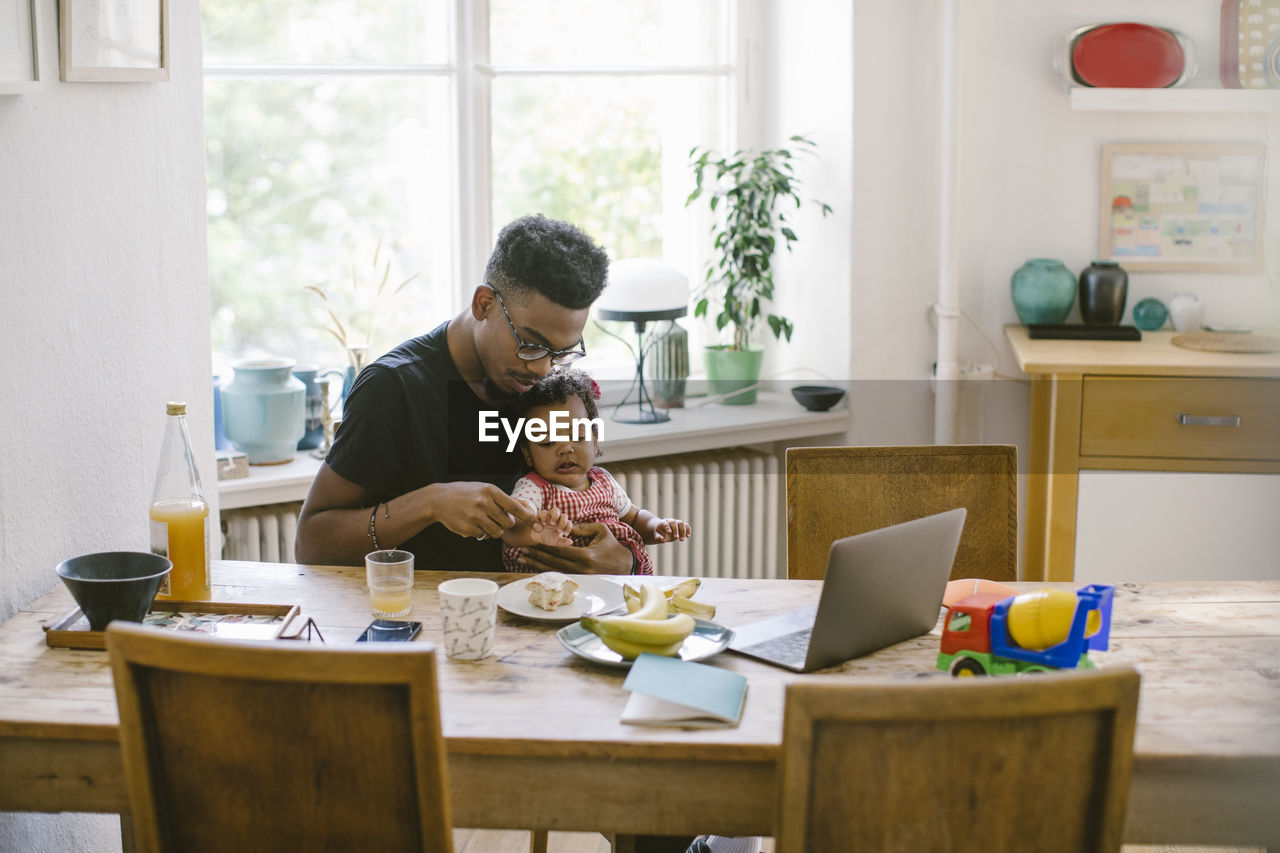 Young man playing with daughter while sitting at table in house